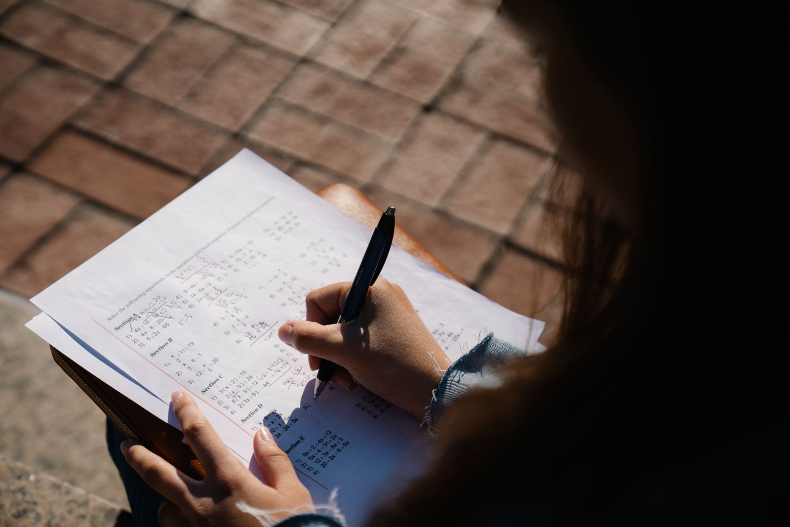 A student working through a printed paper in pen, the questions set out in lettered sections