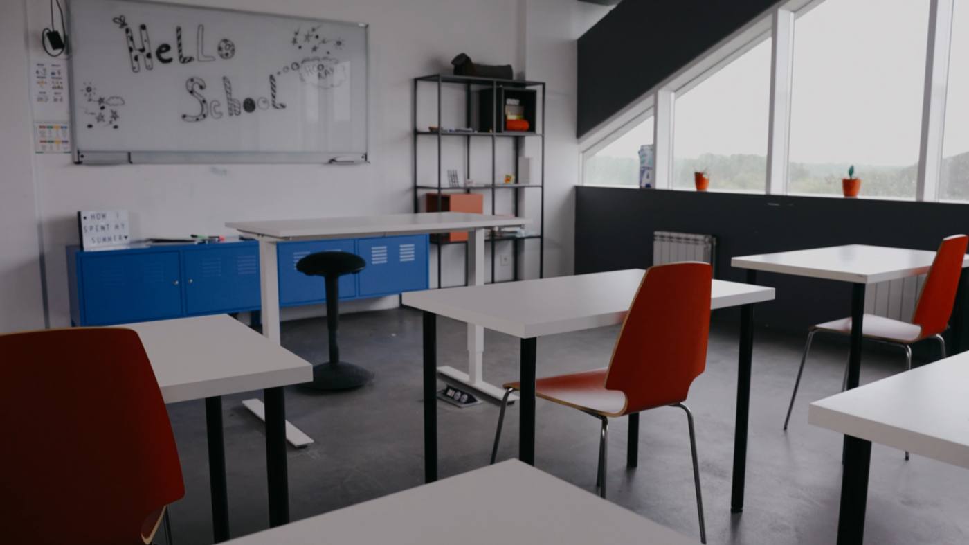 An empty classroom with white tables, red chairs and a whiteboard that reads Hello School